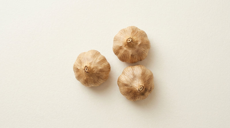 Three whole garlic bulbs arranged on warm cream textured paper.